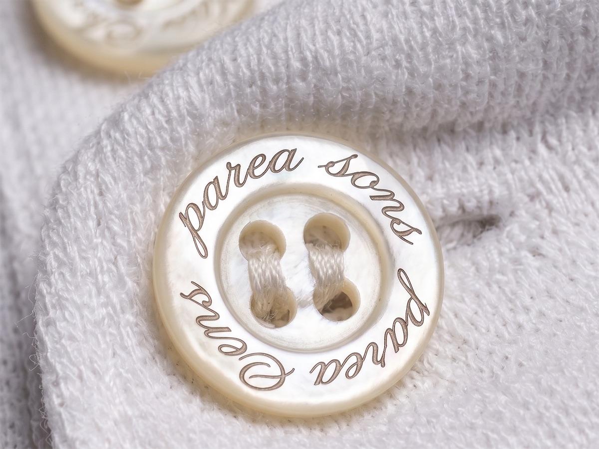 A pale button with “parea sons” engraved around it, sewn onto the linen knit.
