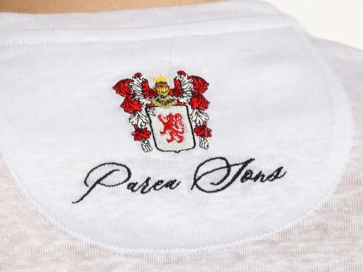 The Parea Sons crest embroidered, seen close up on the white linen knit.