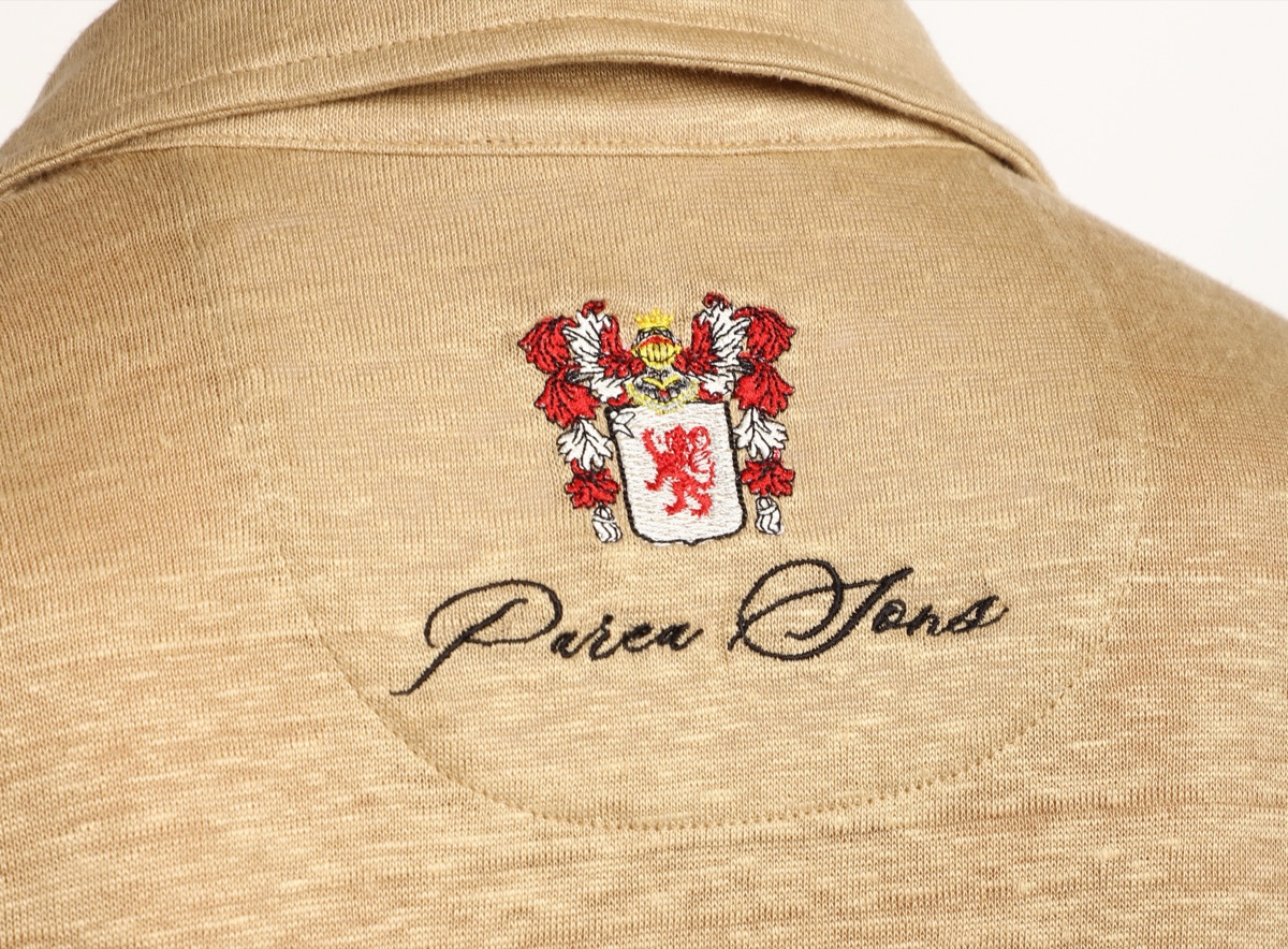A seamstress's hands at work on the embroidery of a crest.